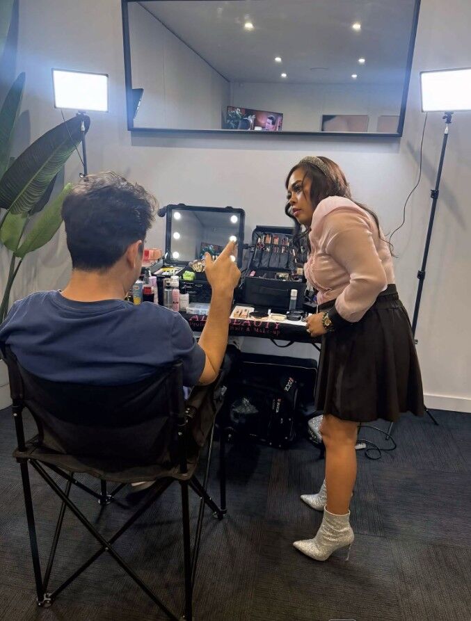 Makeup application backstage at an event, studio lighting rig either side